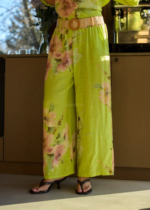 Zielone szerokie spodnie damskie z kwiatowym printem, z wysokim stanem i elastycznym pasem, stylizowane z paskiem i sandałami na obcasie w letnim, świeżym looku.