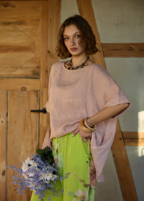 Różowa bluzka lniana damska o luźnym kroju z krótkim rękawem i wiązaniem z tyłu, zestawiona z zielonymi spodniami w kwiaty w naturalnej stylizacji.