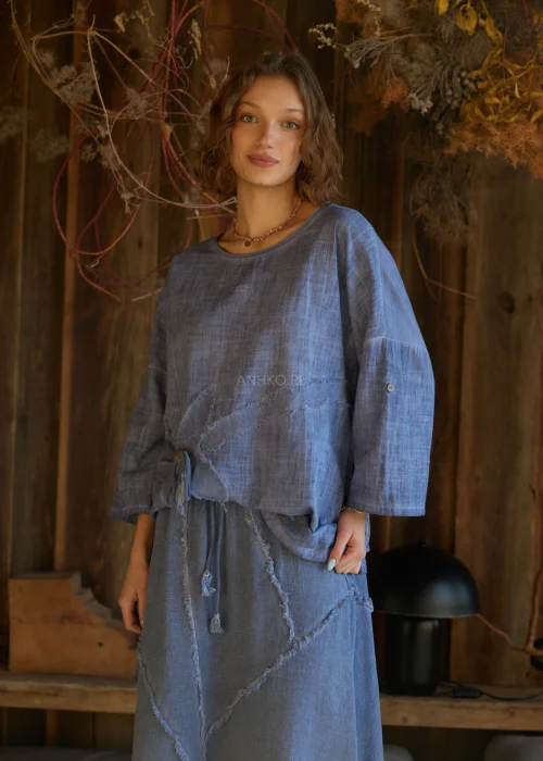 Niebieska bluzka damska o luźnym kroju z długim rękawem, z ozdobnym wiązaniem i surowym wykończeniem detali, w stylu casualowym.