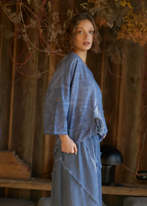 Niebieska bluzka damska o luźnym kroju z długim rękawem, z ozdobnym wiązaniem i surowym wykończeniem detali, w stylu casualowym.