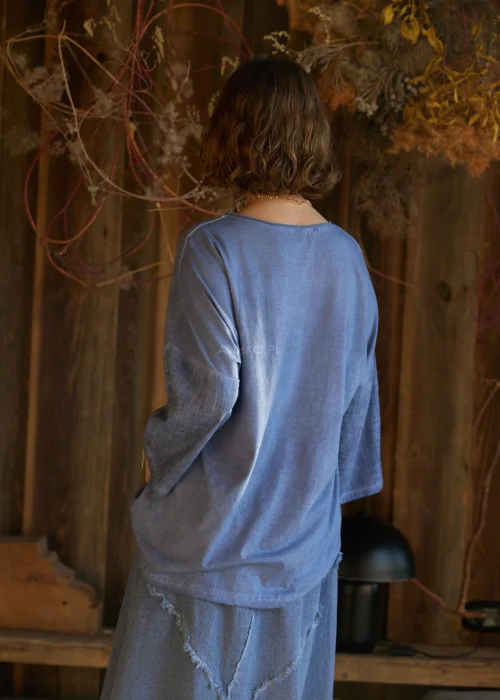 Niebieska bluzka damska o luźnym kroju z długim rękawem, z ozdobnym wiązaniem i surowym wykończeniem detali, w stylu casualowym.