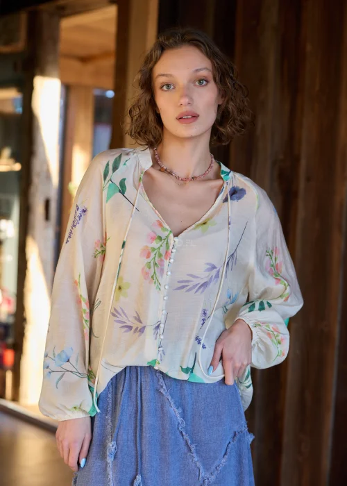 5Bluzka damska w kolorze ecru z delikatnym, wielokolorowym printem roślinnym, o luźnym kroju, z dekoltem V i ozdobnymi guzikami.