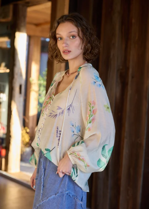 Bluzka damska w kolorze ecru z delikatnym, wielokolorowym printem roślinnym, o luźnym kroju, z dekoltem V i ozdobnymi guzikami.