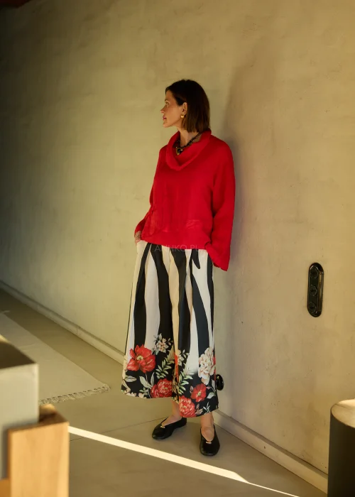 Lniana bluzka damska w intensywnym czerwonym kolorze z długim rękawem i luźnym krojem, dekolt typu komin, stylizacja ze spódnicą w kwiatowy wzór.