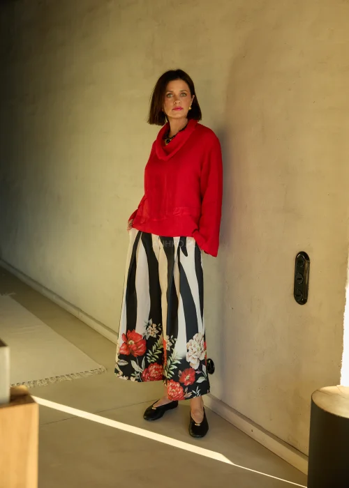 Lniana bluzka damska w intensywnym czerwonym kolorze z długim rękawem i luźnym krojem, dekolt typu komin, stylizacja ze spódnicą w kwiatowy wzór.