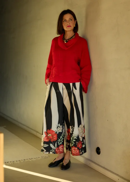 Lniana bluzka damska w intensywnym czerwonym kolorze z długim rękawem i luźnym krojem, dekolt typu komin, stylizacja ze spódnicą w kwiatowy wzór.