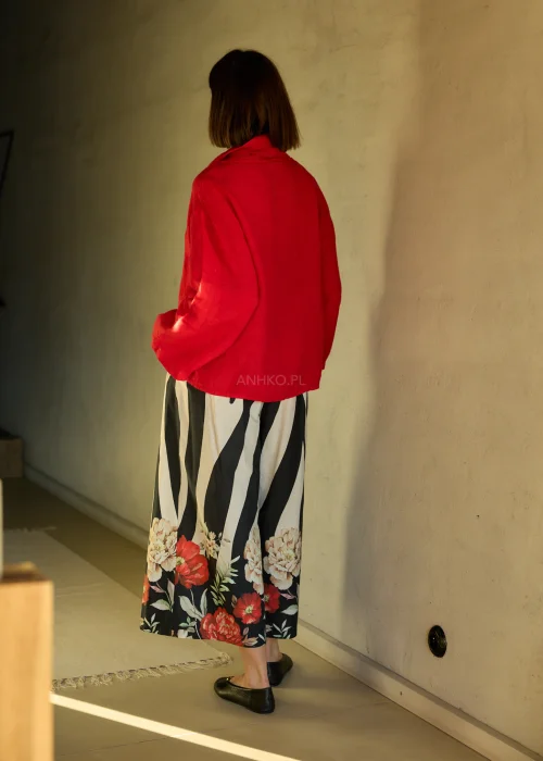 Lniana bluzka damska w intensywnym czerwonym kolorze z długim rękawem i luźnym krojem, dekolt typu komin, stylizacja ze spódnicą w kwiatowy wzór.