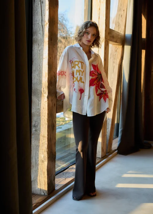 Koszula damska oversize w kolorze białym z dodatkiem lnu, z artystycznym nadrukiem czerwonego kwiatu i napisem, o luźnym kroju i długim rękawie.