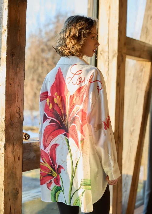 Koszula damska oversize w kolorze białym z dodatkiem lnu, z artystycznym nadrukiem czerwonego kwiatu i napisem, o luźnym kroju i długim rękawie.