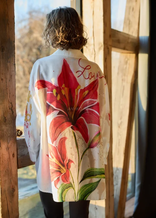 Koszula damska oversize w kolorze białym z dodatkiem lnu, z artystycznym nadrukiem czerwonego kwiatu i napisem, o luźnym kroju i długim rękawie.