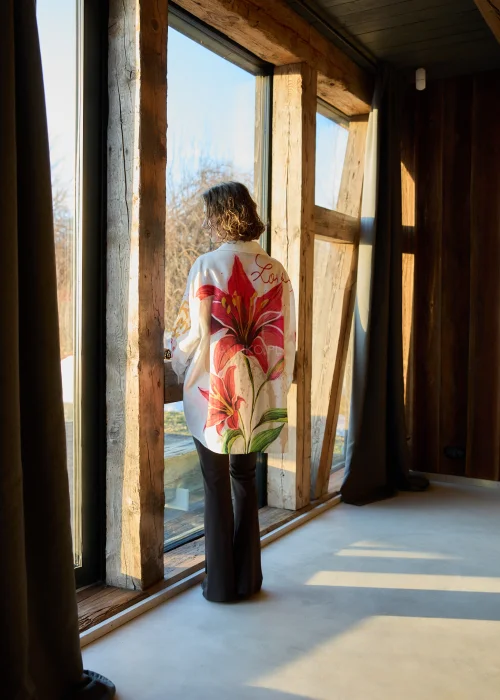 Koszula damska oversize w kolorze białym z dodatkiem lnu, z artystycznym nadrukiem czerwonego kwiatu i napisem, o luźnym kroju i długim rękawie.