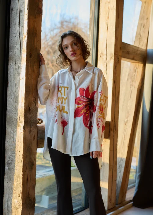 Koszula damska oversize w kolorze białym z dodatkiem lnu, z artystycznym nadrukiem czerwonego kwiatu i napisem, o luźnym kroju i długim rękawie.