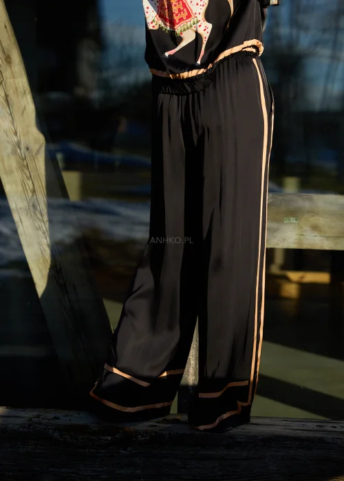 Czarne spodnie damskie z szeroką nogawką i elastyczną talią, ozdobione kontrastowymi brzoskwiniowymi lampasami.