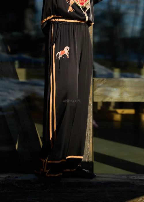 Czarne spodnie damskie z szeroką nogawką i elastyczną talią, ozdobione kontrastowymi brzoskwiniowymi lampasami.