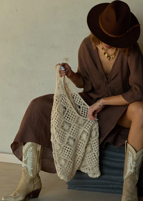 Beżowa torba ażurowa z plecionym wzorem geometrycznym, duża i miękka, noszona na ramieniu w stylizacji boho z sukienką i kapeluszem.