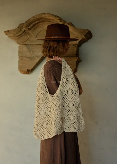 Beżowa torba ażurowa z plecionym wzorem geometrycznym, duża i miękka, noszona na ramieniu w stylizacji boho z sukienką i kapeluszem.