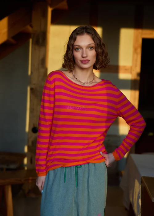 Sweter damski w różowo-pomarańczowe paski z długim rękawem, lekki fason stylizowany z luźnymi spodniami w casualowym looku.