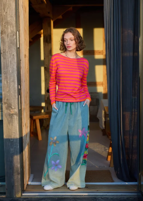Sweter damski w różowo-pomarańczowe paski z długim rękawem, lekki fason stylizowany z luźnymi spodniami w casualowym looku.