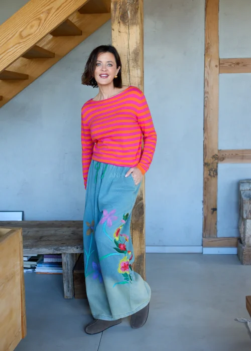 Sweter damski w różowo-pomarańczowe paski z długim rękawem, lekki fason stylizowany z luźnymi spodniami w casualowym looku.