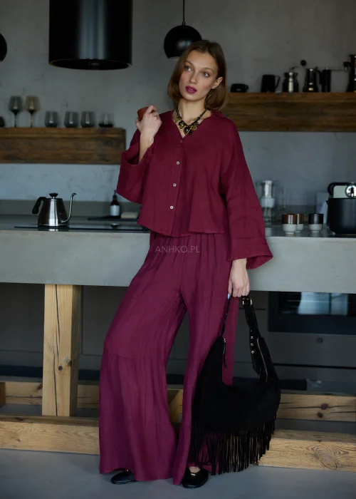 Szerokie spodnie damskie z wysokim stanem w kolorze bordowym, o luźnym kroju z marszczoną talią i rozszerzanymi nogawkami, stylizacja w minimalistycznym, eleganckim klimacie.