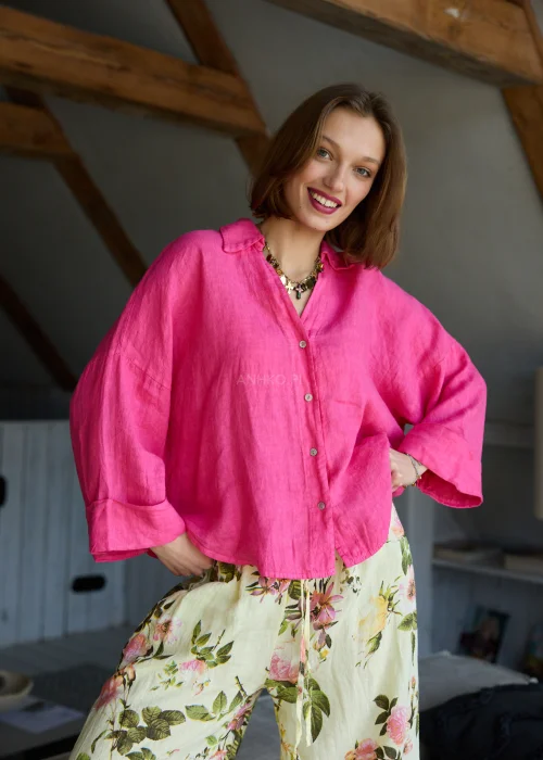 Lniana koszula oversize w odcieniu magenta z długim rękawem i guzikami, o luźnym fasonie, zestawiona z jasnymi spodniami, stylizacja w naturalnym, minimalistycznym klimacie.