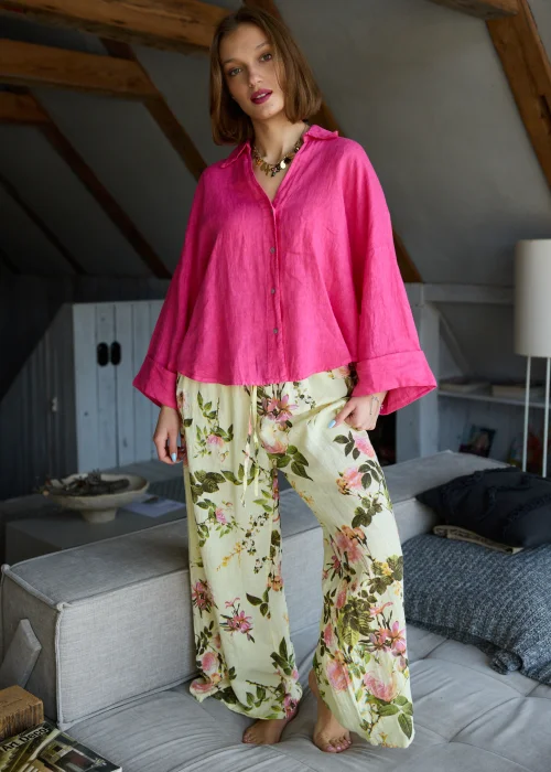 Lniana koszula oversize w odcieniu magenta z długim rękawem i guzikami, o luźnym fasonie, zestawiona z jasnymi spodniami, stylizacja w naturalnym, minimalistycznym klimacie.