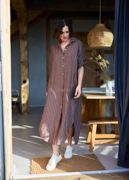 Lniana sukienka koszulowa w brązowym kolorze w tenisowy prążek, o luźnym kroju midi, zapinana na guziki, z kołnierzem i podwijanymi rękawami, tworząca naturalną, swobodną stylizację.