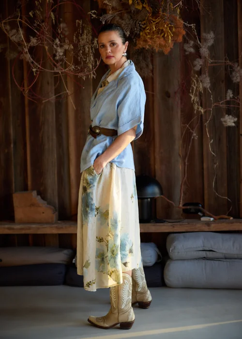 Lniana sukienka koszulowa maxi w beżowym kolorze z delikatnym kwiatowym wzorem, o luźnym kroju z krótkim rękawem i zapięciem na guziki, stylizacja w naturalnym, eleganckim klimacie.