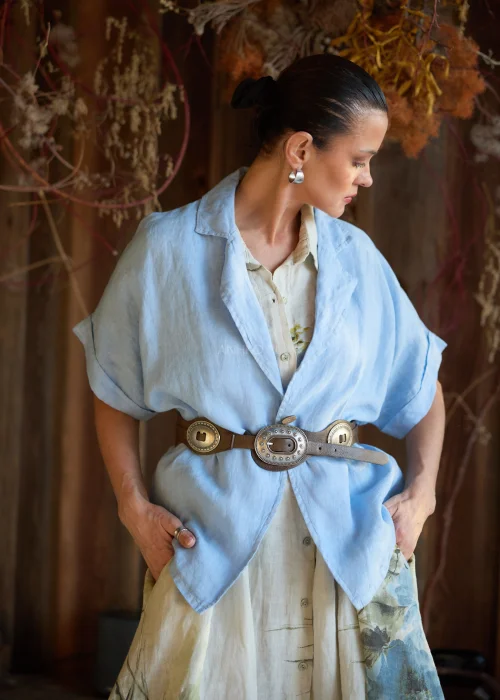 Lniana marynarka damska w kolorze baby blue o luźnym kroju, z krótkim rękawem i klasycznym kołnierzem, stylizacja warstwowa w naturalnym, eleganckim klimacie.