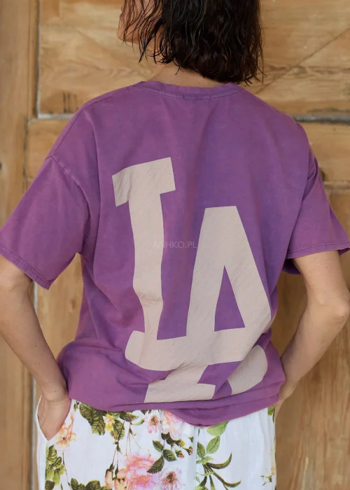 Fioletowa bluzka damska t-shirt o luźnym kroju z nadrukiem „LA” z przodu i dużą grafiką na plecach, w stylizacji casual z kwiatowymi spodniami.