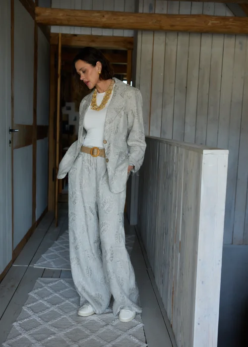Lniana marynarka w szarym kolorze z subtelnym roślinnym wzorem, o luźnym kroju, stylizowana w komplecie ze spodniami w tym samym materiale w eleganckim, naturalnym wydaniu.