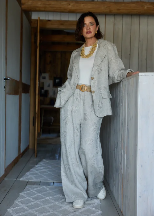 Lniana marynarka w szarym kolorze z subtelnym roślinnym wzorem, o luźnym kroju, stylizowana w komplecie ze spodniami w tym samym materiale w eleganckim, naturalnym wydaniu.