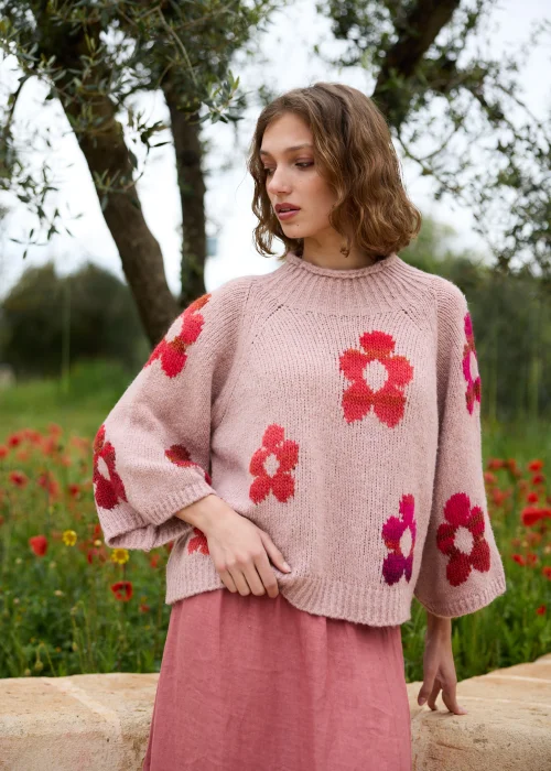 Sweter pudroworóżowy z kolorowym motywem kwiatów w odcieniach różu, czerwieni i fuksji. Miękki fason z szerokimi rękawami dodaje stylizacji przytulnego, kobiecego charakteru