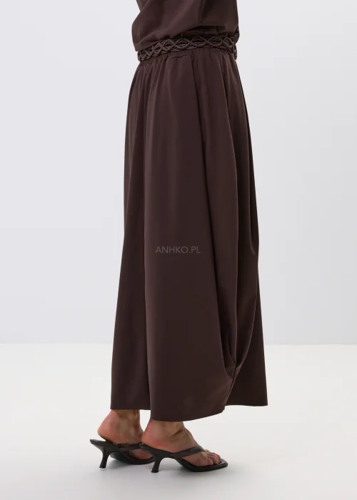 Brązowa spódnica maxi z elastyczną talią i ozdobnym paskiem. Lekko drapowany fason pięknie układa się w ruchu i dodaje stylizacji nowoczesnej elegancji.