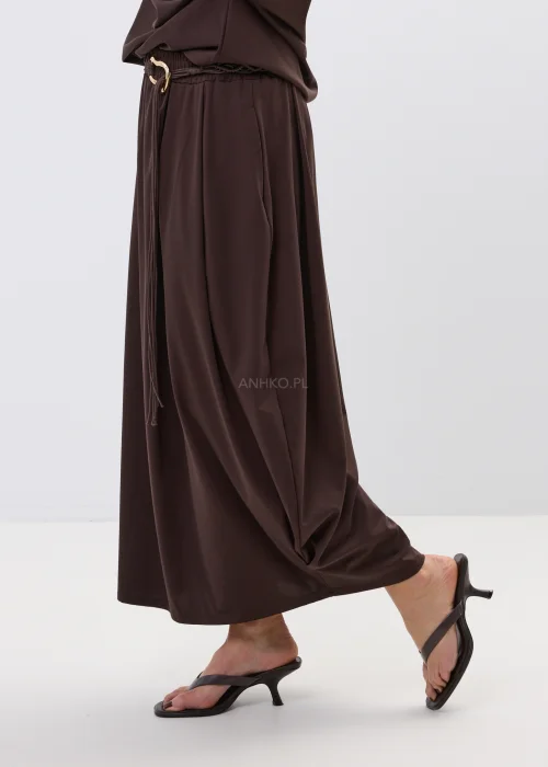 Brązowa spódnica maxi z elastyczną talią i ozdobnym paskiem. Lekko drapowany fason pięknie układa się w ruchu i dodaje stylizacji nowoczesnej elegancji.