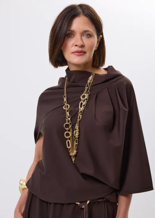 Brązowa bluzka o nowoczesnym, asymetrycznym fasonie z efektownym układaniem przy dekolcie. Miękko opływa sylwetkę i nadaje stylizacji eleganckiego charakteru.