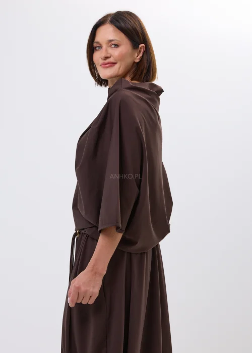 Brązowa bluzka o nowoczesnym, asymetrycznym fasonie z efektownym układaniem przy dekolcie. Miękko opływa sylwetkę i nadaje stylizacji eleganckiego charakteru.