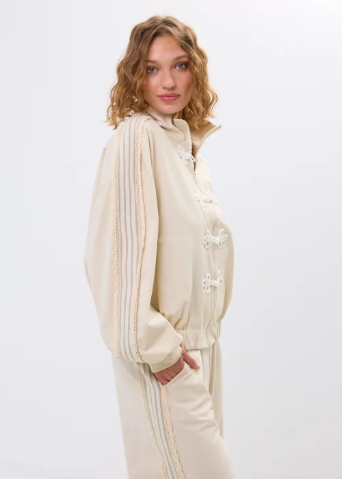 Beżowa bluza oversize na zamek z ozdobnymi wiązaniami i wysokim kołnierzem. Luźny fason nadaje stylizacji nowoczesny i oryginalny charakter.