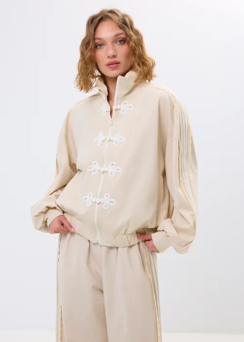 Beżowa bluza oversize na zamek z ozdobnymi wiązaniami i wysokim kołnierzem. Luźny fason nadaje stylizacji nowoczesny i oryginalny charakter.