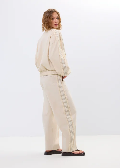 Beżowa bluza oversize na zamek z ozdobnymi wiązaniami i wysokim kołnierzem. Luźny fason nadaje stylizacji nowoczesny i oryginalny charakter.