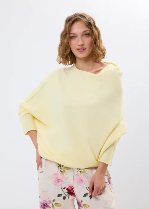 Masełkowy sweter damski oversize z miękkiej dzianiny i szerokim dekoltem typu boat neck. Lekki sweter w pastelowym odcieniu zestawiony z kwiatowymi spodniami w kobiecej casualowej stylizacji.