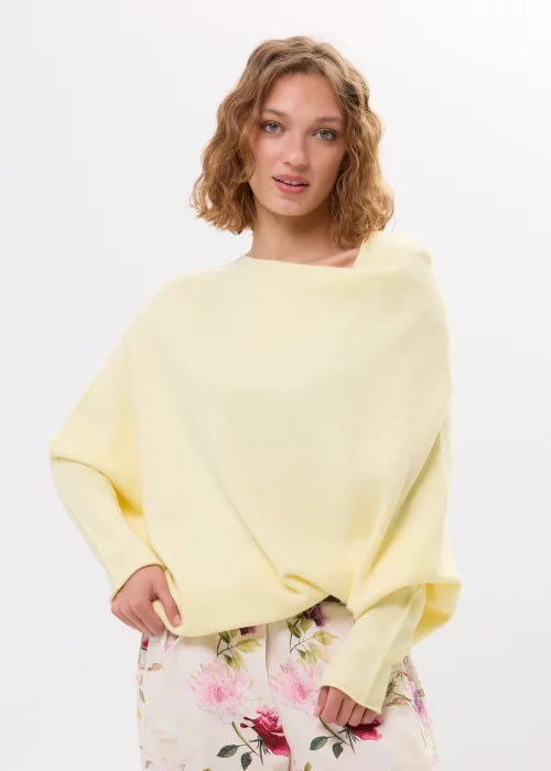 Masełkowy sweter damski oversize z miękkiej dzianiny i szerokim dekoltem typu boat neck. Lekki sweter w pastelowym odcieniu zestawiony z kwiatowymi spodniami w kobiecej casualowej stylizacji.