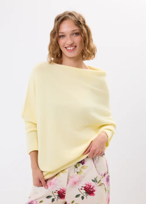Masełkowy sweter damski oversize z miękkiej dzianiny i szerokim dekoltem typu boat neck. Lekki sweter w pastelowym odcieniu zestawiony z kwiatowymi spodniami w kobiecej casualowej stylizacji.