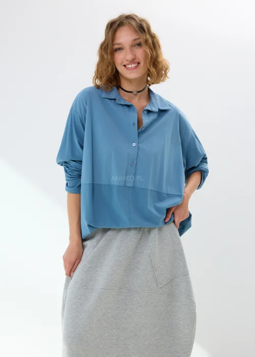 Niebieska koszula damska oversize z kołnierzem i guzikami z przodu, wykonana z bawełny z dodatkiem elastanu. Model zestawiony ze wzorzystą spódnicą w stylizacji miejskiej.