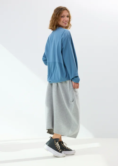 Niebieska koszula damska oversize z kołnierzem i guzikami z przodu, wykonana z bawełny z dodatkiem elastanu. Model zestawiony ze wzorzystą spódnicą w stylizacji miejskiej.