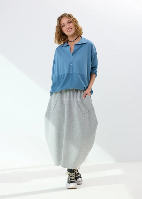 Niebieska koszula damska oversize z kołnierzem i guzikami z przodu, wykonana z bawełny z dodatkiem elastanu. Model zestawiony ze wzorzystą spódnicą w stylizacji miejskiej.
