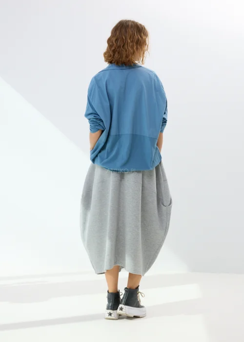 Niebieska koszula damska oversize z kołnierzem i guzikami z przodu, wykonana z bawełny z dodatkiem elastanu. Model zestawiony ze wzorzystą spódnicą w stylizacji miejskiej.