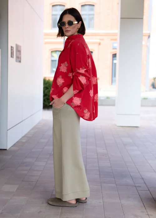 Damska czerwona koszula oversize z różanym printem, kieszenią na piersi i podwijanymi rękawami. Elegancka stylizacja z oliwkową spódnicą podkreśla kobiecy, nowoczesny charakter outfitu.