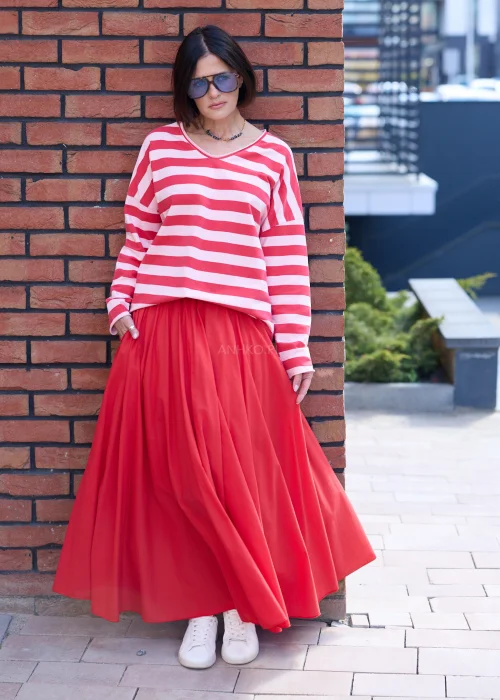 Damska czerwona spódnica maxi o rozkloszowanym fasonie z elastyczną talią i lekko lejącym materiałem. Stylizacja z bluzką w paski i sportowymi sneakersami podkreśla swobodny, miejski charakter outfitu.