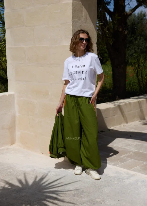 Biały T-shirt damski z nadrukiem „I Have Nothing To Wear” w czarnym kolorze. Luźny model casual zestawiony z zielonymi spodniami i okularami przeciwsłonecznymi.